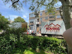 Twee verhuiswagens van "Professional Moving Company" met een verhuislift bij een appartementencomplex op een zonnige dag.
